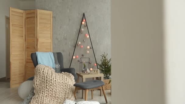 Élégant intérieur scandinave de Noël avec un fauteuil élégant et des mérinos chauds. Maison confort avec décor nordique du nouvel an. Arbre de Noël minimaliste avec guirlandes et lumières dans la pièce lumineuse . — Video