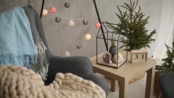 Elegante interior escandinavo de Navidad con un elegante sillón y cálidos merinos a cuadros. Hogar confortable con decoración nórdica de año nuevo. Árbol de Navidad minimalista con guirnaldas y luces en la sala de luz . — Vídeos de Stock