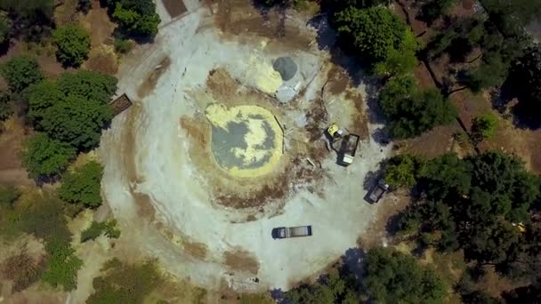 Der gelbe Bagger gräbt den Boden der Baugrube aus und bringt die Ladung mit einer Schaufel zum LKW. Erdarbeiten auf der Brunnenbaustelle. 4k Luftaufnahmen vom Wiederaufbau des Parks. — Stockvideo