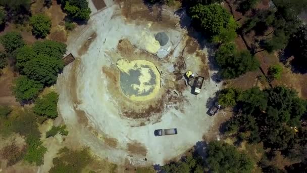 Gele graafmachine graaft grond van Stichting pit en behandeling lading met een emmer naar de truck. Grondwerk voorbereiding op de bouwplaats fontein. 4 k luchtfoto beelden van park wederopbouw. — Stockvideo