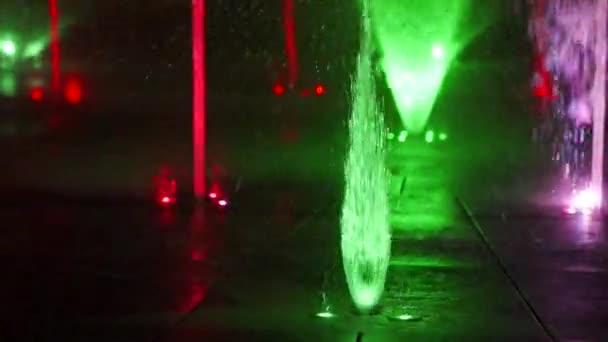 Цветной танцевальный фонтан ночью. Медленный съёмка крупным планом струй воды на тёмном фоне. Силуэты неузнаваемых людей . — стоковое видео
