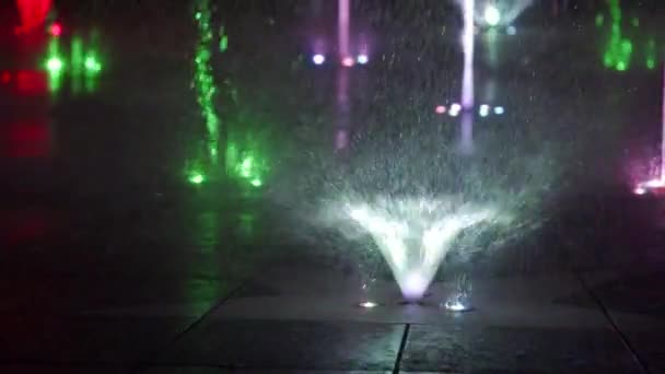 Värikäs tanssiva suihkulähde yöllä. Hidasliikkeisiä lähikuvia vesisuihkuista tummalla pohjalla. Tunnistamattomat ihmiset siluetit . — kuvapankkivideo
