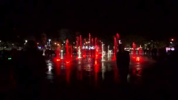 カラフルな噴水ショー夜。暗い背景に水のジェット機のスローモーション映像。認識できない人々 のシルエット. — ストック動画