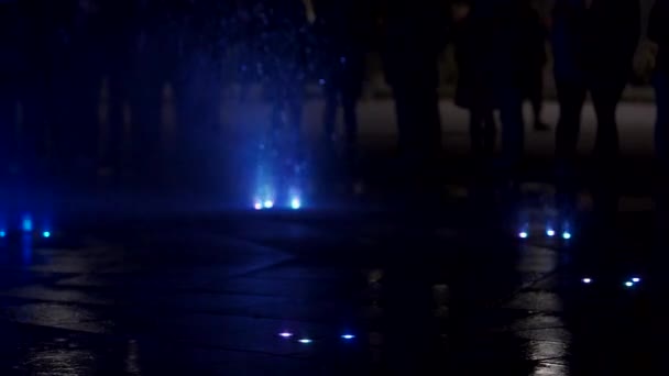 Цветной танцевальный фонтан ночью. Медленный съёмка крупным планом струй воды на тёмном фоне. Силуэты неузнаваемых людей . — стоковое видео