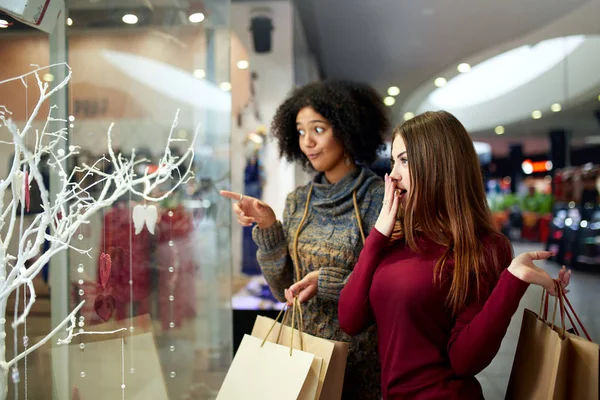 Kağıt Poşetler yakınındaki bir şekilde dekore edilmiş shopwindow ile genç çok ırklı farklı yarış bayanlar. Tarafından parmak shopfront, giyim ve alışveriş merkezi yılbaşı yeni yıl satış ürünleri dönük kız.