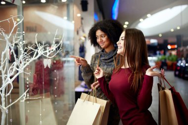 Kağıt Poşetler yakınındaki bir şekilde dekore edilmiş shopwindow ile genç çok ırklı farklı yarış bayanlar. Tarafından parmak shopfront, giyim ve alışveriş merkezi yılbaşı yeni yıl satış ürünleri dönük kız.