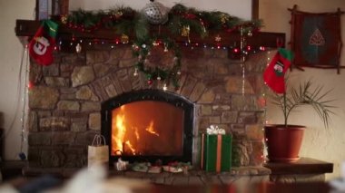 Yangın yanık içinde bir şömine Noel arifesinde garland ışıklar, çelenk, çorap ve hediye kutuları ile dekore edilmiştir. Yeni yıl tatilleri kutlama. 1080 p Full Hd çekim dolly.