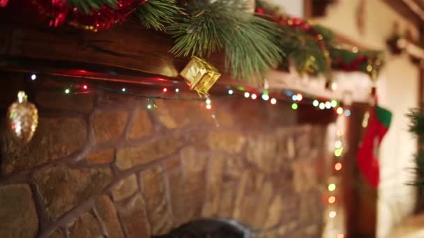 Hombre en suéter apuñalado colgando corona de Navidad sobre piedra auténtica chimenea decorada con luces de guirnalda intermitentes de colores. Año Nuevo vacaciones preparación y decoración. Vista cercana dolly shot . — Vídeo de stock