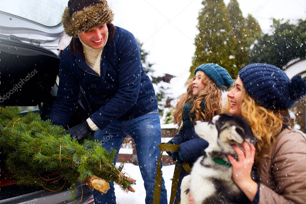 Father brought christmas tree in trunk of SUV car to daughter, mother and dog to decorate home. Family prepares for new year together. Large boot space concept. Snowy winter outdoors