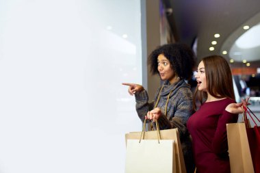 Kağıt Eko poşetler yakınındaki beyaz shopwindow boşaltmak için tasarımcı ile genç çok ırklı farklı yarış bayanlar. Tarafından parmak shopfront, giyim ve alışveriş merkezinde ürünleri dönük kız.