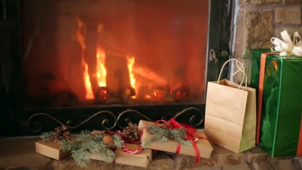 Рождественские подарки украшены еловыми ветвями, шишками, лентами, лежащими у камина. Теплый дровяной огонь. Рождественское утро, когда Санта принес украшенные коробки с подарками. Новогодние праздники . — стоковое видео