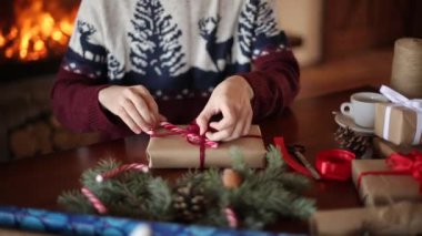 Yakın görünümünü şömine yakın Noel tatili için bir hediye olarak bir yay bağlama eller mans. Kağıt koniler, çam dalları ile dekorasyon, erkek kaydırma mevcut kutulara ahşap masa üzerinde şeker kamışı.