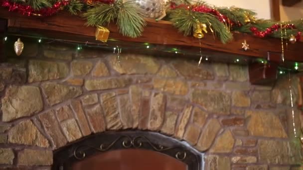 Hombre en suéter apuñalado colgando corona de Navidad sobre piedra auténtica chimenea decorada con luces de guirnalda intermitentes de colores. Año Nuevo vacaciones preparación y decoración. Vista media dolly shot . — Vídeos de Stock