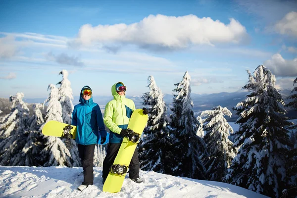 Dos snowboarders posando en la estación de esquí. Jinetes amigos llevando sus tablas de snowboard a través del bosque para freeride backcountry y con gafas reflectantes, traje de moda de colores. Área del espacio de copia . —  Fotos de Stock