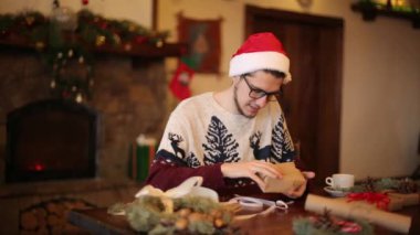 Mutlu bir adam Noel hediye kutusu şömine yakınındaki garland yanıp sönen ile açılış santa şapka giymiş. Gülümseyen adam hediyeleri ve zevk/açma paket ile bir paket aldı. Kış tatil kavramı.