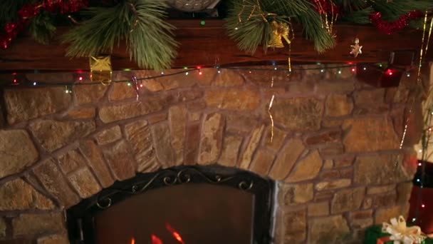 Hombre en suéter apuñalado colgando corona de Navidad sobre piedra auténtica chimenea decorada con luces de guirnalda intermitentes de colores. Año Nuevo vacaciones preparación y decoración. Vista cercana dolly shot . — Vídeos de Stock