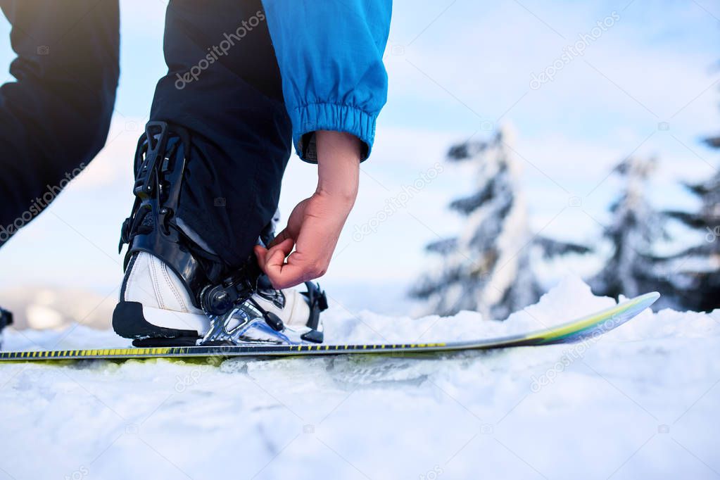 Snowboarder straps in his legs in snowboard boots in modern fast flow bindings with straps. Rider at ski resort prepares for freeride session. Man wearing fashionable outfit.