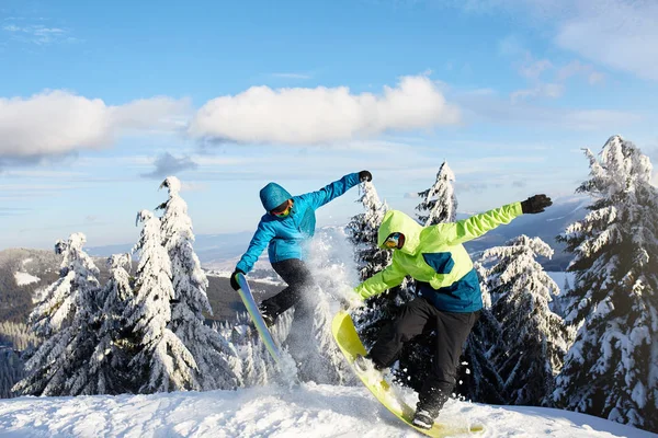 Dos snowboarders haciendo trucos en la estación de esquí. Jinetes amigos realizando salto con sus tablas de snowboard cerca del bosque en sesión freeride backcountry en traje de moda de colores. Área del espacio de copia . —  Fotos de Stock