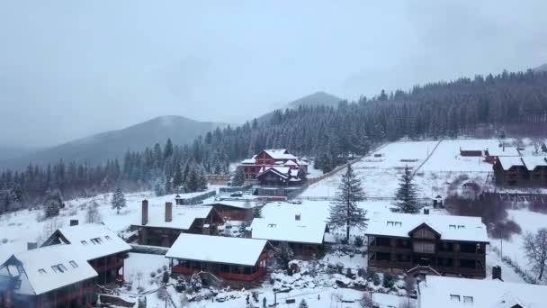겨울에 산에 살고 있는 지역의 항공 사진 산 마 건물 들과 눈 덮인 언덕 사면에 눈으로 덮여 있다. 시골, 전나무 나무와 소나무 숲입니다. 스키장의 코 티 지. — 비디오