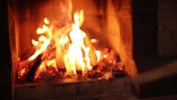 Young stylish man in knitted sweater throwing wooden logs in fireplace at home. Unrecognizable caucasian male puts wood in the stove hearth in wooden cottage. Guy drowns a fire in his house. — Stock Video