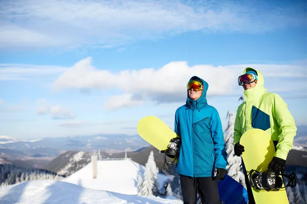 Dos snowboarders posando en la estación de esquí. Jinetes amigos llevando sus tablas de snowboard a través del bosque para freeride backcountry y con gafas reflectantes, traje de moda de colores. Área del espacio de copia . —  Fotos de Stock