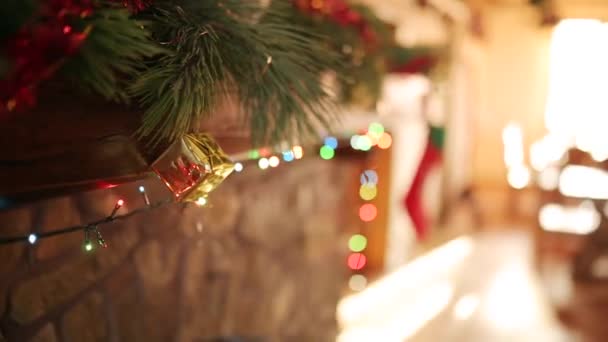Hombre en suéter apuñalado colgando corona de Navidad sobre piedra auténtica chimenea decorada con luces de guirnalda intermitentes de colores. Año Nuevo vacaciones preparación y decoración. Vista cercana dolly shot . — Vídeos de Stock