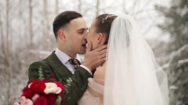Yeni evliler damat ve gelin öpücük ve kontur birbirlerine karlı herdem yeşil orman içinde ağır çekimde kar yağışı sırasında sarıl. . Romantik Çift kış ormanda. Buket kadınla. Sevgililer günü ve Noel.