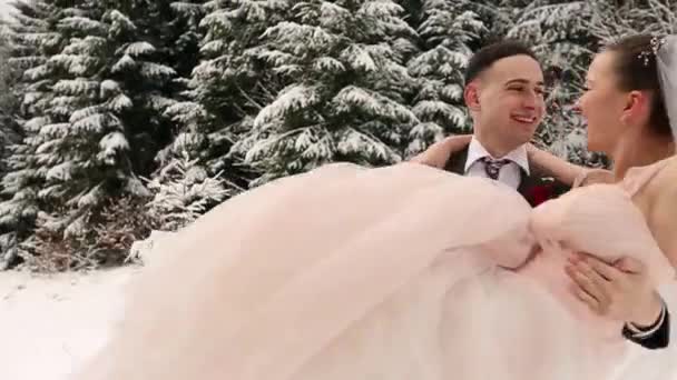 Γαμπρός κλώση ευτυχισμένη νύφη κρατώντας και νηματοποίηση της στα χέρια του στο χιόνι καιρός ερυθρελάτης ελατοδάσος κατά τη διάρκεια της χιονόπτωσης. Ευτυχισμένος νεόνυμφους να διασκεδάσουν. Γυναίκα με μπουκέτο. Ημέρα του Αγίου Βαλεντίνου Χριστούγεννα έννοια. — Αρχείο Βίντεο