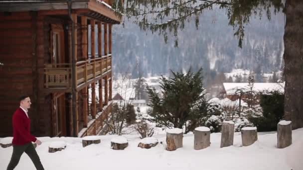 Der Bräutigam kommt zur Braut, umarmt und küsst sie im verschneiten Bergdorf im Skigebiet. romantisches Hochzeitspaar in gestrickten Marsala-Pullovern bei Schneefall im Winter. Weihnachten und Valentinstag. — Stockvideo
