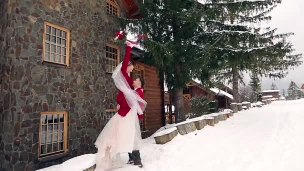 Groom spinning happy bride holding and spinning her in his hands in snow weathernear ski resort village cottage. Happy newlyweds have fun. Woman with bouquet. Valentines Day Christmas concept. — Stock Video