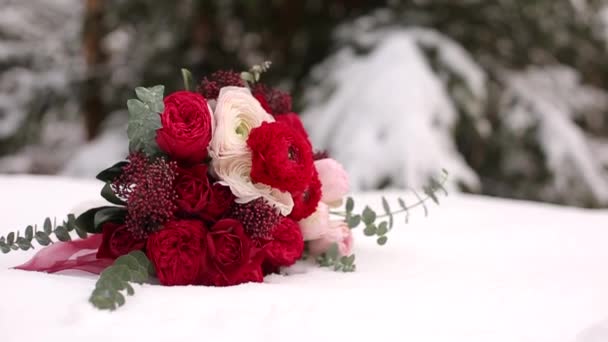 Svatební kytice z červených a bílých květin na sněhu v lesích jehličnatých conferous. Zavřít a makro pohled Nabídková růže na zasněženém povrchu během sněžení v smrkových zimním lese. — Stock video