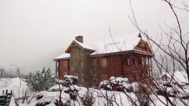 Dağ köyü ile iğne yapraklı orman arka plan üzerinde yoğun kar yağışı sırasında tahta kulübede. Kar günlüğü chalets adlı Kayak Merkezi düşüyor. Soğuk soğuk kış günü dağlarda. Ağır çekim.