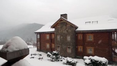 Dağ köyü ile iğne yapraklı orman arka plan üzerinde yoğun kar yağışı sırasında tahta kulübede. Kar günlüğü chalets adlı Kayak Merkezi düşüyor. Soğuk soğuk kış günü dağlarda. Ağır çekim.