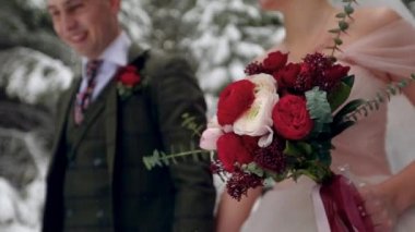 Gelin buket çiçek taşıyan beyaz ve kırmızı gül yaptı. Evlilik çift tutuşup karlı ormanda kar yağışı sırasında yürüyüş. Kış düğün ilham. Damat ve gelin masal ormanda.