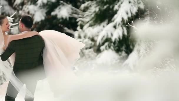 Sposo filatura sposa felice tenendo e girando lei nelle sue mani in neve tempo abete foresta abete rosso durante la nevicata. Gli sposi felici si divertono. Donna con bouquet. Concetto di Natale di San Valentino . — Video Stock
