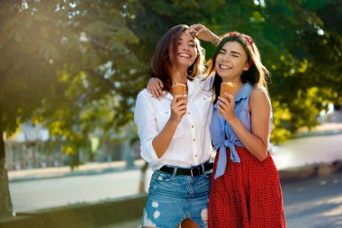 Eğleniyor ve dondurma yemek iki genç arkadaşlar. Dondurma açık havada şehirde yemek neşeli beyaz kadın. Güzel kızlar dondurma ile poz. Yaz saati kavramı.