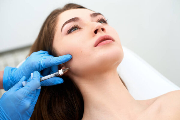 Beautician doctor with filler syringe making injection to jowls. Masseter lines reduction and face contouring therapy. Anti-aging treatment and face lift in cosmetology clinic. Patient lying on chair