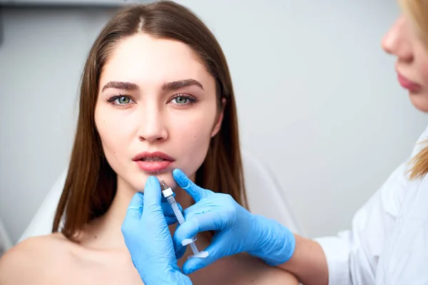 Lip Augmentation. Closeup Of Beautician Doctor Hands Doing Beauty Procedure To Female Lips with Syringe. Young Womans Mouth Receiving Hyaluronic Acid Injection. Cosmetology Treatment. Mesotherapy.