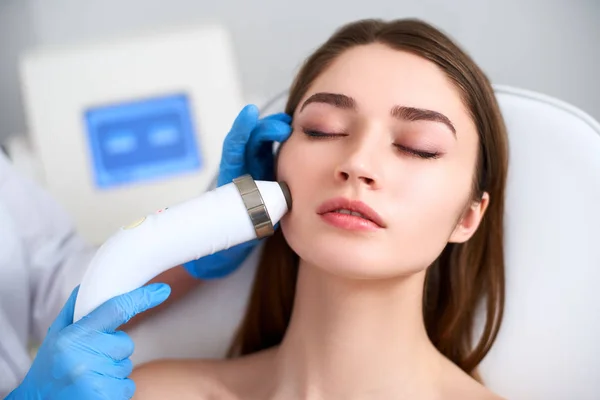 Beautician doctor doing rf-lifting procedure for flawless woman face laying in a beauty salon. Hardware cosmetology. Patient receiving electric facial massage. Skin rejuvenation and wrinkle smoothing. — Stock Photo, Image