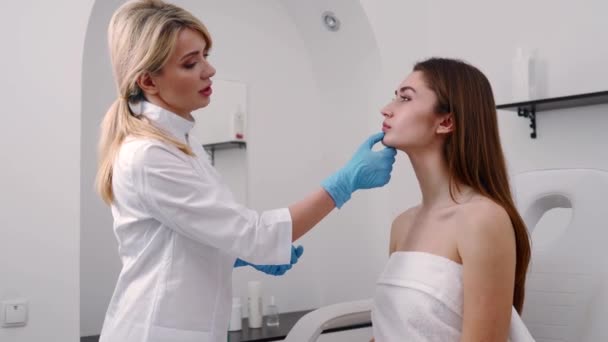 Cirujano plástico o especialista en cosmetología examina la cara de las mujeres, toca con las manos, inspecciona la piel curada después de la cirugía con resultados increíbles. Cliente sentado en chequeo en médico adjunto . — Vídeo de stock