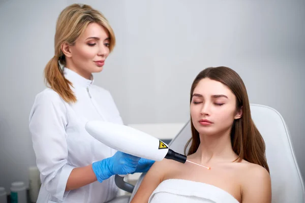 Extracción de lunares láser en el pecho de una mujer en un salón de belleza. Cosmetología de hardware. Guapa rubia esteticista médico quitando marca de nacimiento o nevus con pistola láser en salón de belleza . —  Fotos de Stock