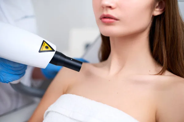 Laser mole removal on a womans chest in a beauty salon. Hardware cosmetology. Beautician doctor removing birthmark or nevus with laser beam gun in beauty salon. Patient laying on medical chair.
