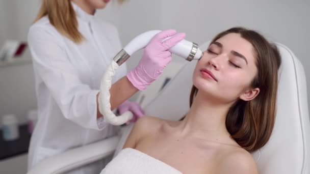 Guapa rubia esteticista médico haciendo rf-lifting procedimiento para la mujer acostada en un salón de belleza. Cosmetología de hardware. Paciente recibiendo masaje facial eléctrico. Rejuvenecimiento de la piel y alisamiento de arrugas . — Vídeos de Stock