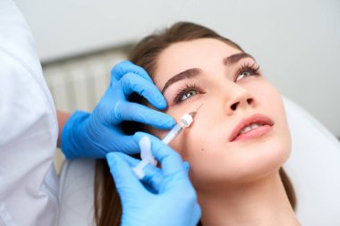 Şırınga ile tıbbi eldiven Doktor gençleştirici kırışıklık tedavisi için gözlerin altında botulinum enjekte. Göz kırışıklıkları için dolgu enjeksiyonu yumuşatma. Güzellik kliniğinde plastik estetik yüz cerrahisi