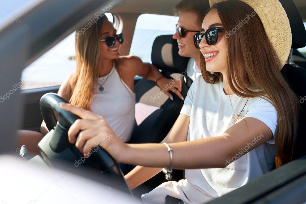 Friends rented a car for summer road trip to the beach. Female driver in glasses and straw hat having fun. Woman learned car driving and got a license. Girl wearing teeth braces. Travel lifestyle.