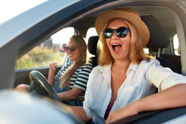 Deniz plajına tatil gezisi bir arabada iki genç neşeli gülümseyen kadın. Gözlüklü kız tatillerde kiralık bir araç kullanıyor. Yaz keyfini Kız arkadaşları tatilde okyanus kıyısına geldi.