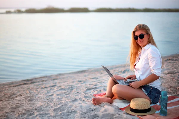 Authentic woman working with laptop on sea shore. Freelancer girl telecommuting with team on project on tropical island. Female using internet from computer while sitting on beach towel on sunset. — Stock Photo, Image