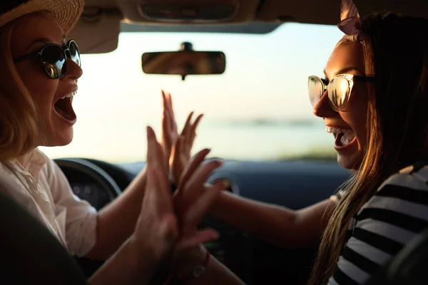 Blij opgewonden jonge vrouwen rijden in de auto en het maken van hoge vijf gebaar op zomer vakantie reis. Twee meisjes verheugen ze aangekomen bij Destination Beach. Vakantie in de buurt van de zee of de Oceaan. Zomer Lifestyle. — Stockfoto