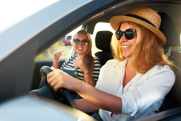 Две молодые веселые улыбающиеся женщины в машине во время отпуска на морском пляже. Девушка в очках за рулем автомобиля от аренды в праздничные дни. Подружки, наслаждающиеся летом, приезжают в отпуск на побережье океана . — стоковое фото