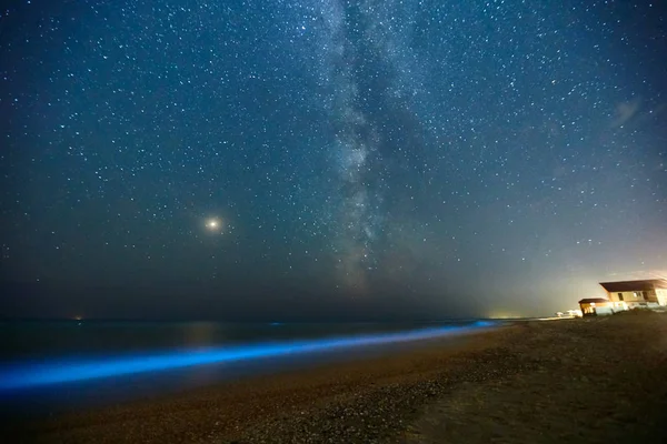 Long exposure shot of glowing plankton on sea surf and milky way. Blue bioluminescent glow of water under the starry sky. Rear nature phenomenon. Bright Mars planet among constellations in night sky. — Stock Photo, Image